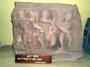 Táncoló Ganésa, a hindi nyelvű felirat szerint banszurín (fuvola) és mridangán (dob) játszó táncosokkal. Madhya Pradesh, 10. század. Dr. Harisingh Gour Archaeological Museum of Sagar University, Sagar (Madhya Pradesh)
