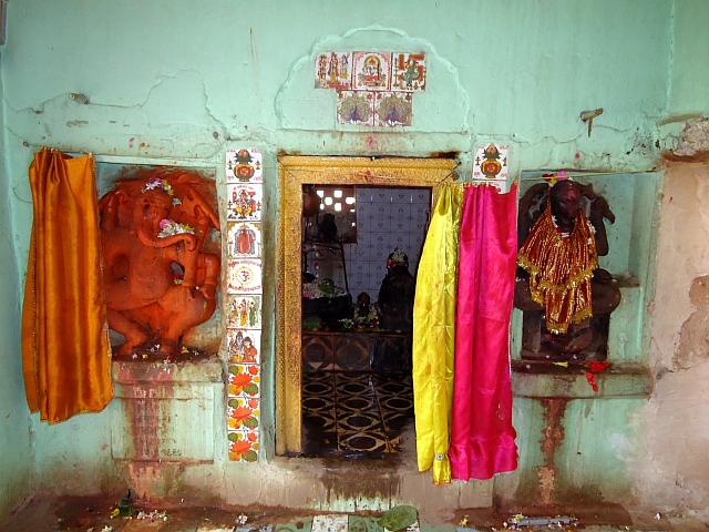 Narancsvörösre festett táncoló Ganésa a Visnu-Varáha templom egyik mellékszentélye bejáratánál. Régi templom helyén épült újkeletű építmény, de a szobrok többsége eredeti. Madhya Pradesh, Majhauli (Jabalpur District), Kalacsuri-korszak, kb. 11. század. Ganésa mellett a csempéken szerencsejelek sorakoznak. Fentről lefelé haladva 1. bőségkorsó napkereszttel (szvasztika, =”jó-lét”, azaz bőség, jószerencse) és szerencsekívánsággal: शुभ लाभ śubh lābh/subh-lábh, =”boldogságot, hasznot”, azaz sok szerencsét! 2. Még egy Ganésa, „Üdv, tisztelet Ganésának!” felirattal. 3. Ez Ganésa Ganapatiként. Ganésa és Ganapati ugyanazt jelenti: a ganák, azaz Siva seregének ura. 4. Gájatrí mantra, nagy szentségnek örvendő védikus ima. 5. Nehezen kivehető, de valószínűleg Visnu, Laksmí, Garuda és egy kísérő. 6. Siva a háromágú szigonyával, Párvatíval és Ganésával. 7. Vízililiomok, azaz lótuszok. Az indiai vallásokban a lótusz tisztaság szimbóluma. 